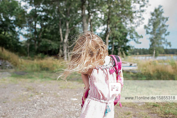 junges blondes Mädchen  das einen Rucksack anzieht  während der Wind ihr die Haare weht