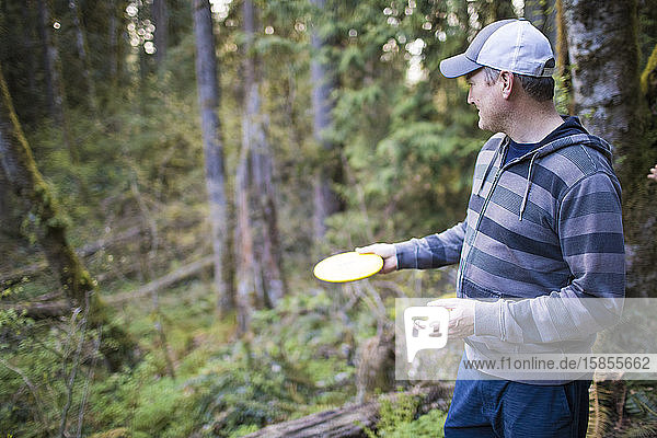 Mann bereitet sich darauf vor  während eines Scheibengold-Spiels im Wald Frisbee zu werfen.