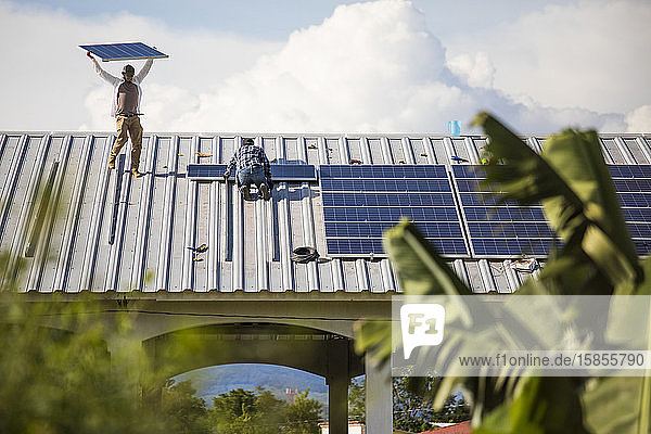 Zwei Männer installieren nachhaltige Sonnenkollektoren in Reihen auf dem Dach.