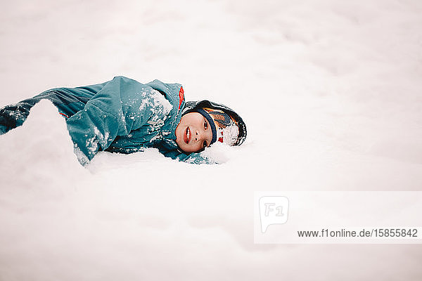 Glücklicher Junge liegt im Winter im Schnee