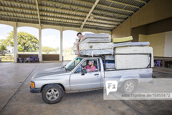 Zwei Männer  die auf einem beladenen Lastwagen mitfahren  helfen beim Transport von Matratzen im Waisenhaus.