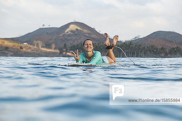 Smiling young woman lying on surfboard
