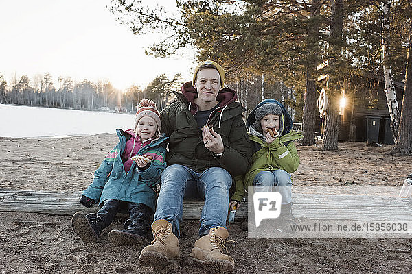 Vater und seine Kinder essen im Winter gemeinsam Hot Dogs am Strand
