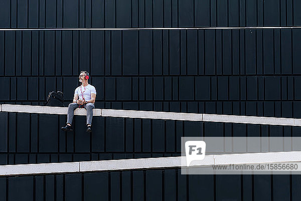 Mature man sitting on a wall listening to music with headphones