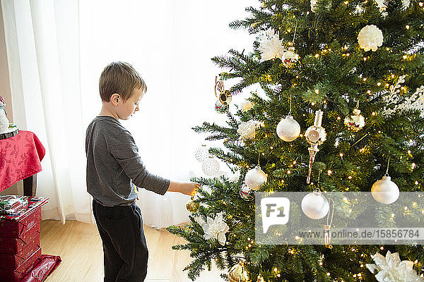 Junge steht und legt während der Feiertage Ornament auf den Weihnachtsbaum