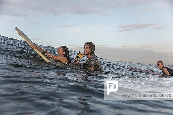 Glückliche Freunde mit Surfbrettern und Kamera im Meer