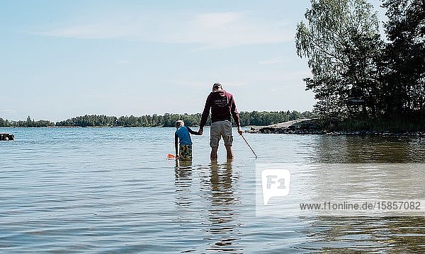 Vater hält die Hand seines Sohnes  während er mit einem Netz im Meer fischt