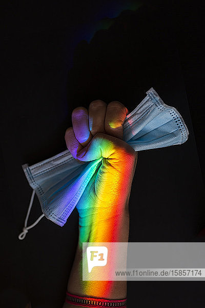 Symbol einer geschlossenen Frauenfaust mit einem Regenbogen, der eine Hygienemaske zusammendrückt. Covid-19