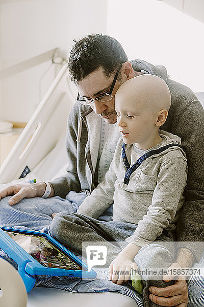 Father recovering from surgery watches tablet with son in hospital