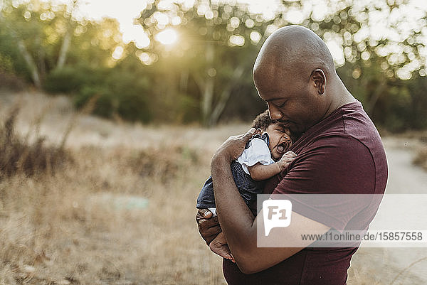 Close up of sweet father cuddling newborn girl in backlit field