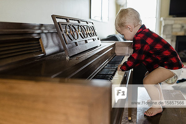 Baby boy in diaper stands on bench playing piano at home