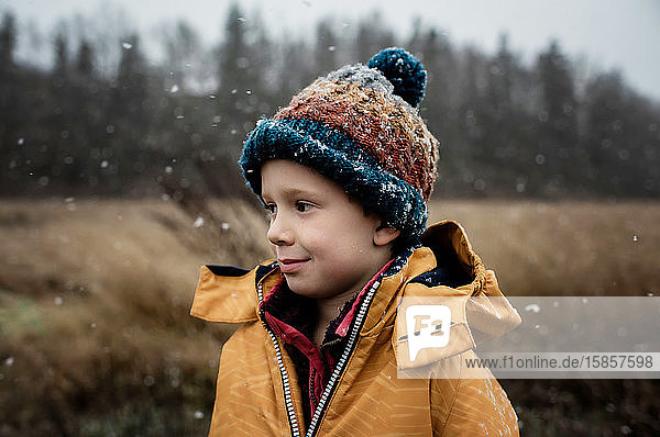Porträt eines Jungen  der im Schnee steht und im Winter lächelt