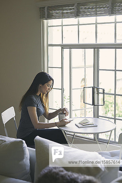 Woman using mobile phone while having coffee at table in living room