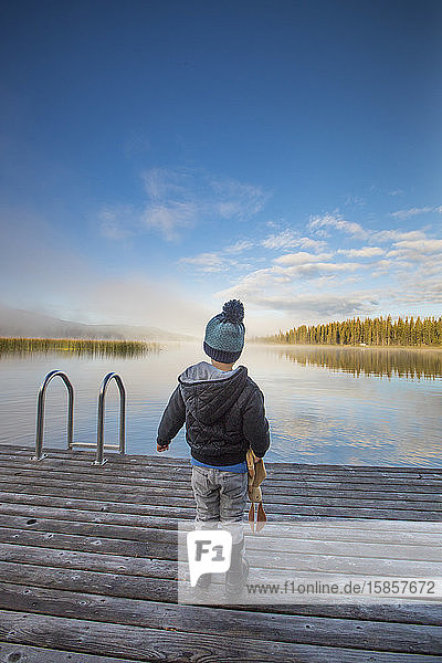 Young boy standing on wooden dock at the lake.