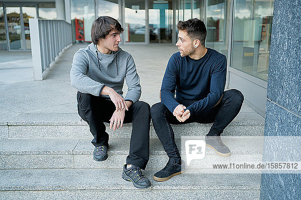Frontansicht von zwei jungen Männern  die auf einer Stadttreppe sitzend reden und