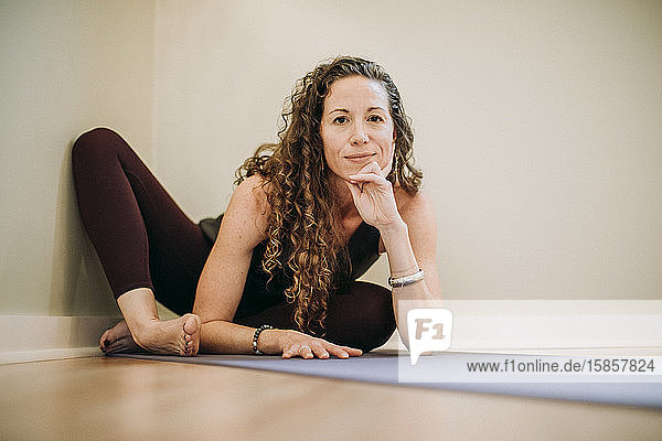 fit woman with curly hair relaxes on yoga mat in corner of studio