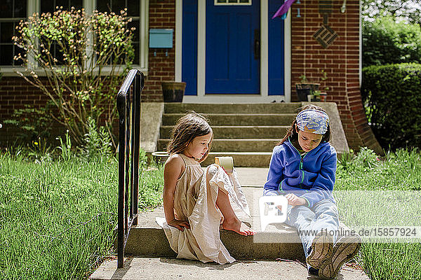 Zwei kleine Mädchen sitzen im Sonnenschein auf der Vorderbeuge und unterhalten sich miteinander