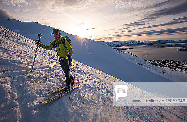 Skifahrender Mann in Island bei Sonnenaufgang mit Wasser hinter sich