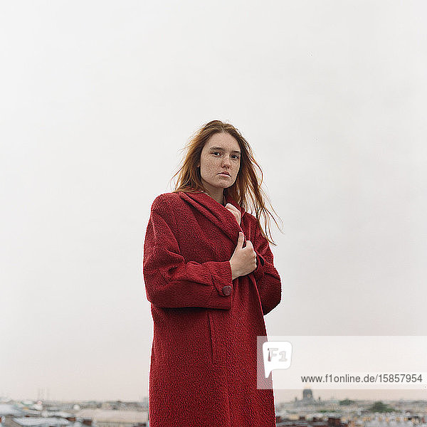 Bildnis einer schönen brünetten Frau in rotem Mantel auf dem Dach stehend