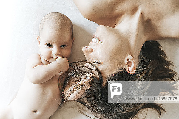 Mutter und neugeborener Sohn liegen ausgestreckt im Bett  der Sohn fängt die Haare der Mutter  und sie schaut ihn mit Liebe an