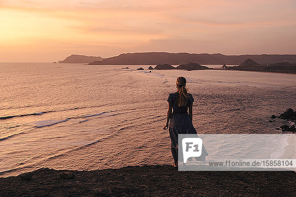 Junge Frau an der Küste bei Sonnenuntergang