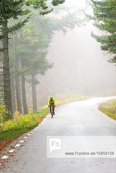 gesunder Mann  der an einem nebligen Tag auf einer Bergstraße Fahrrad fährt