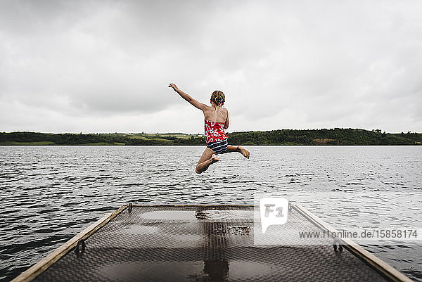 Kleines Mädchen springt an einem bewölkten Sommertag vom Dock in den See