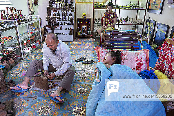 Ein vietnamesischer Handwerker arbeitet  während seine Tochter ihn auslacht.