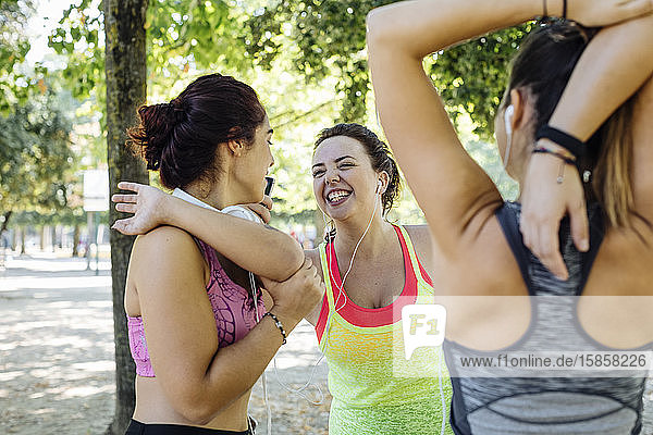 Junge Freundinnen lachen beim Aufwärmtraining im Park