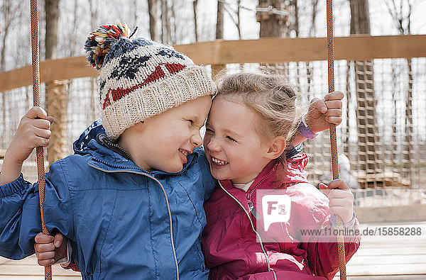 Mädchen und Junge auf einer Schaukel  die zusammen draußen spielen und lachen
