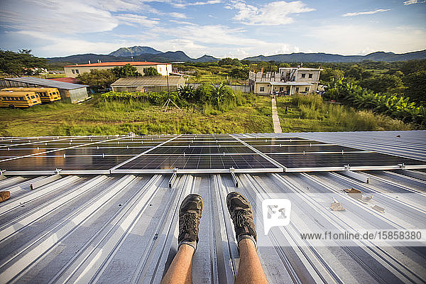 Hochwinkelansicht der Beine der Arbeiter und der installierten Sonnenkollektoren vom Dach aus.