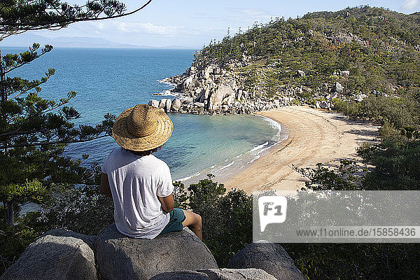 Curly hair man with hat and swimsuit  on top of rock  admiring the bay