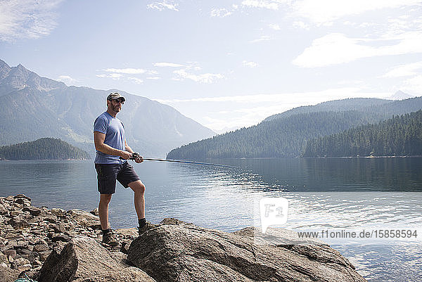 Mann steht auf Felsen und angelt am Ross Lake im Bundesstaat Washington