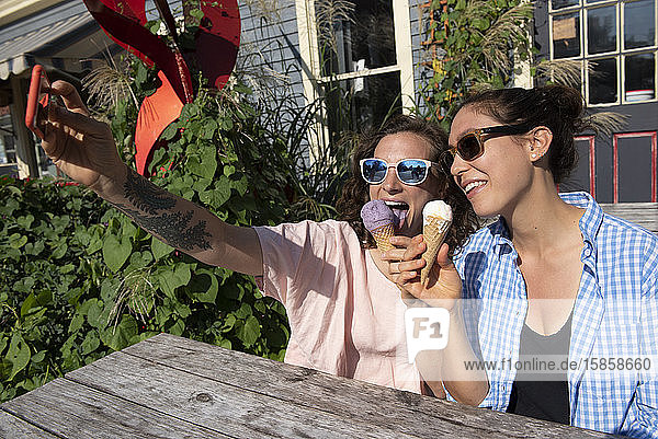Zwei Frauen genießen einen Sommertag indem sie beim Eisessen ein Selfie machen und lächeln.