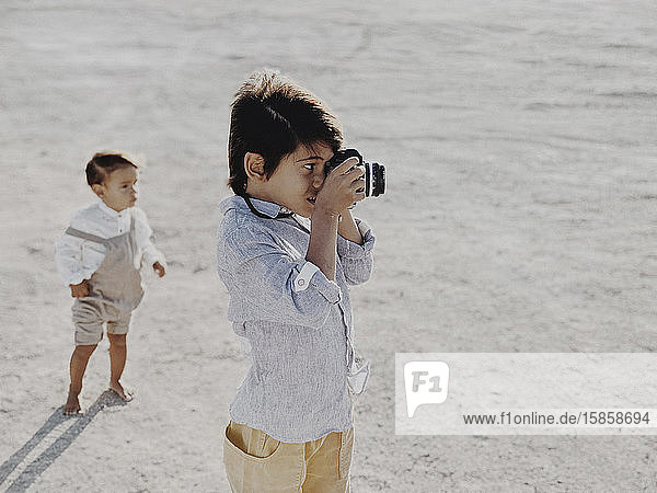 Kind fotografiert mit einer Oldtimer-Kamera  während ein anderes Kind im Hintergrund steht
