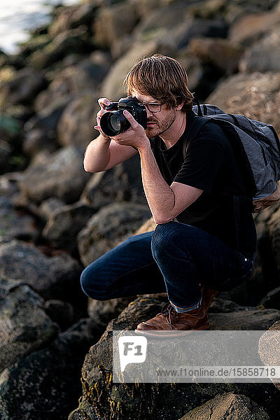Junger Mann beim Fotografieren in der Hocke auf Stein
