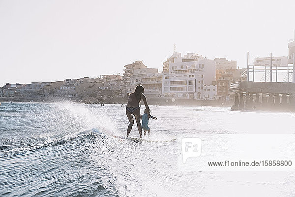 Pulled back view of mother and son surfing a small wave at sea