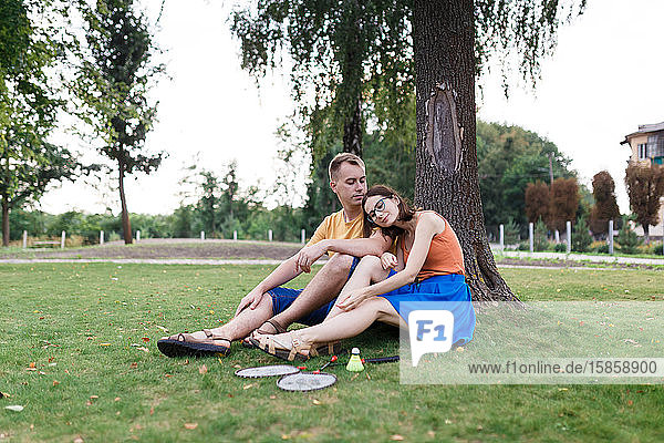 Millennial couple sitting in the grass after playing badminton in the park
