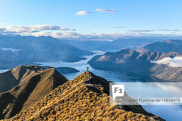 Mann steht auf Berggipfel mit Blick auf blauen See in Neuseeland.