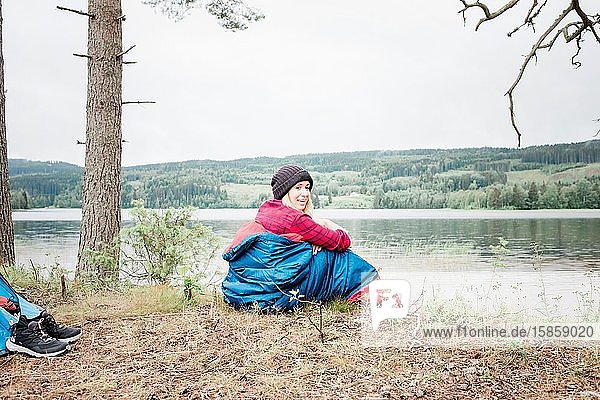 Frau lacht  während sie beim Camping in Norwegen in einem Schlafsack sitzt