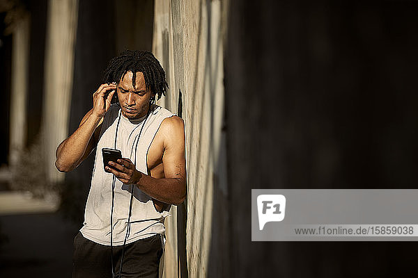 African-American man looking at phone adjusting earbuds