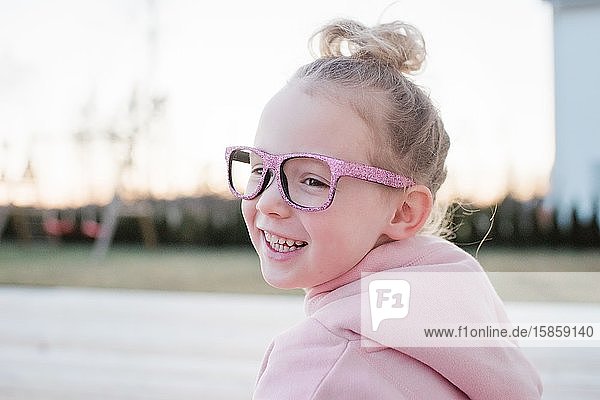 portrait of a young girl with a bun and pink sparkly glasses on