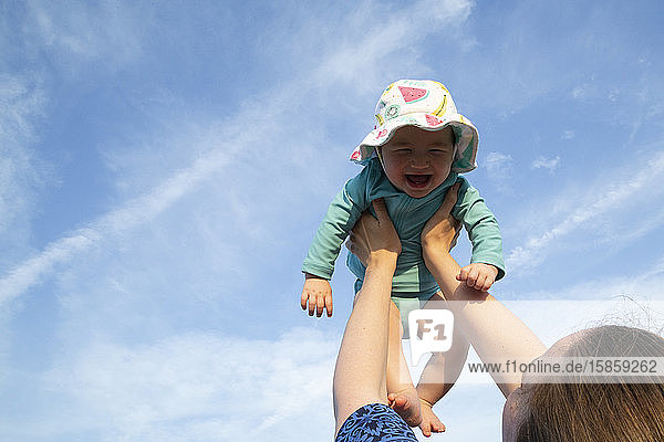Mother holding baby girl up in air with both arms against a blue sky