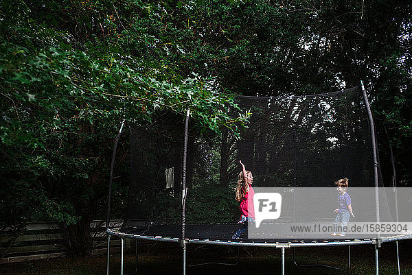 Ein Mädchen und ein Junge springen auf einem Trampolin im Freien.