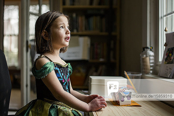 Ein kleines Kind spielt in einem Prinzessinnenkostüm am Fenster und schaut auf