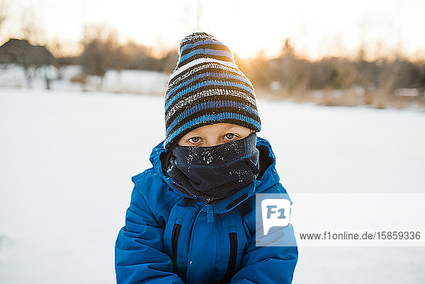 Young boy looking at camera with blue scarf and winter hat.