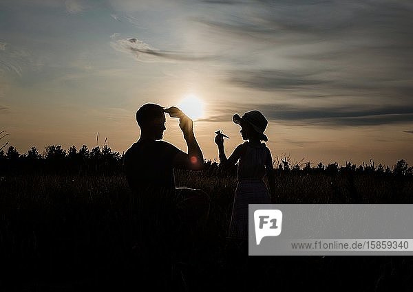 Silhouette eines Vaters und einer Tochter  die draußen mit einem Papierflugzeug spielen