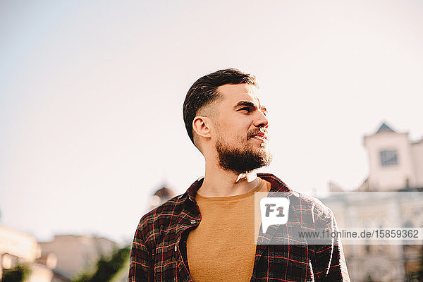 Porträt eines selbstbewussten jungen Hipster-Mannes vor klarem Himmel in der Stadt