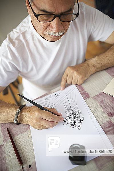 Älterer Mann zeichnet mit Feder.