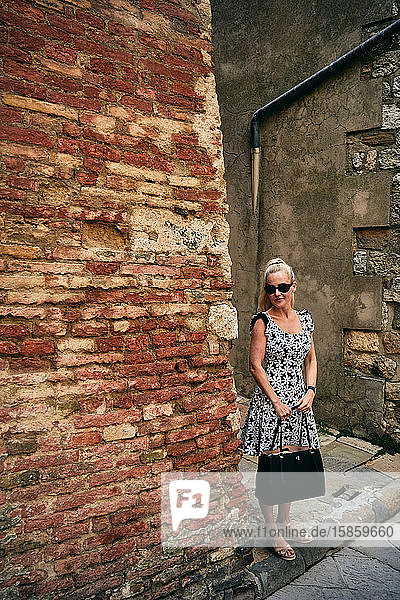 Stilvolle reisende Frau mit Tasche steht neben alter gemauerter Wand